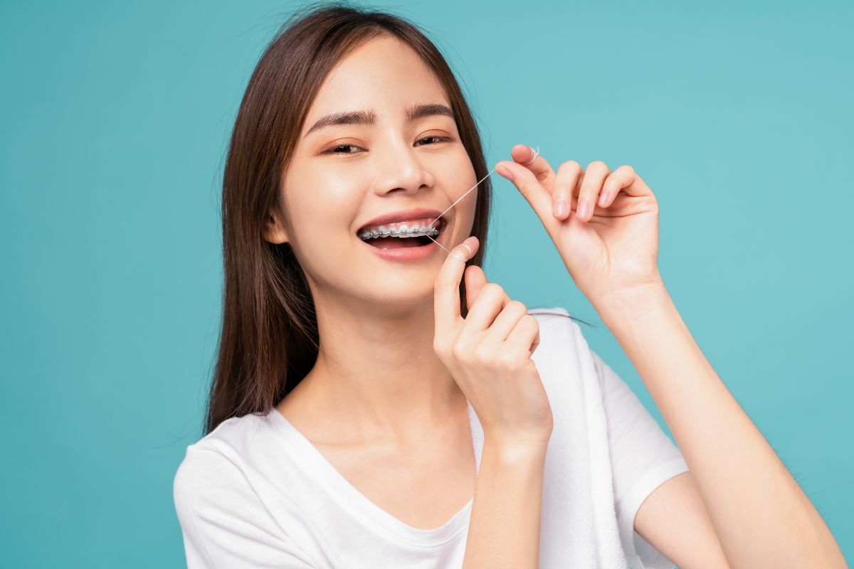 Flossing with Braces Young woman with braces flossing teeth against turquoise background, smiling happily.