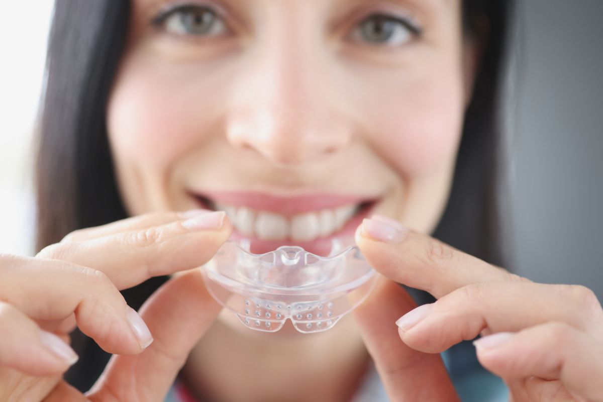 Do You Need a Mouthguard for Braces Woman holding clear orthodontic aligner tray, smiling, displaying teeth whitening or straightening treatment.