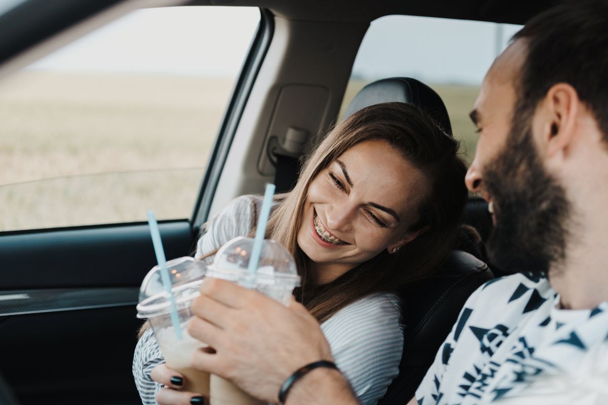 Traveling with New Braces Young couple enjoying beverages inside a car during a road trip, smiling together.