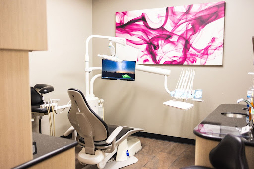 Modern dental office operatory with chair, equipment, monitor, and pink abstract artwork on wall.
