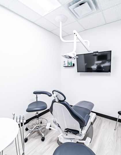 4eef33dc-img Modern dental operatory with chair, overhead light, monitor, and clinical equipment in white treatment room.