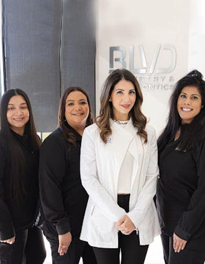 dc63e073-blvd-dentistry-orthodontics-image2 Four women smiling at camera in professional office setting with BLVD branding visible on wall.