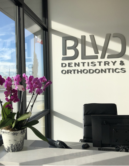 fa6baa21-img-3 BLVD Dentistry & Orthodontics reception desk with purple orchids and modern interior signage.