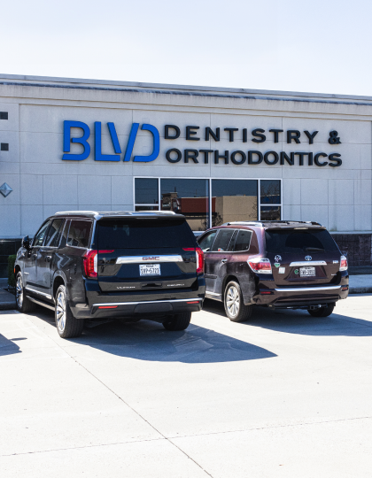 Two SUVs parked in front of BLVD Dentistry & Orthodontics storefront building.