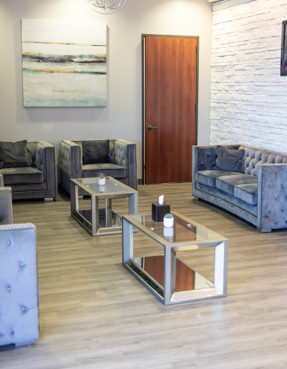 Modern waiting room with upholstered seating, wooden coffee table, and contemporary artwork on white brick walls.