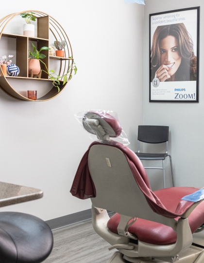 Modern dental office with burgundy chair, circular wall shelf, and Philips Zoom whitening advertisement poster.
