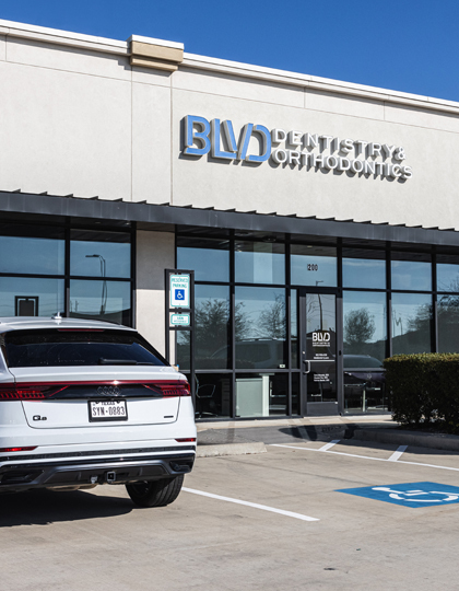 4c8a1dd5-slider-image-new-2 BUD Dentistry storefront with white SUV parked in front on clear day.