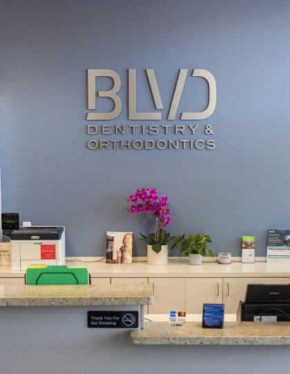 img-blvd-dentistry—orthodontics2 BLVD Dentistry & Orthodontics reception desk with logo, flowers, and welcome items on shelves.