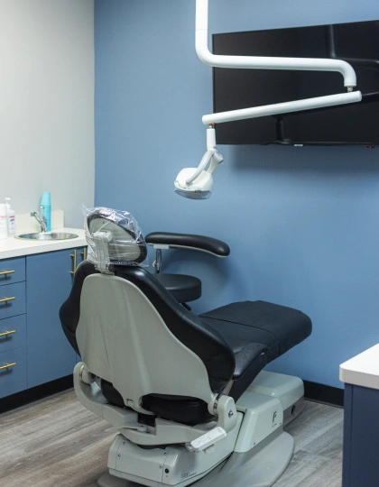 img-blvd-dentistry—orthodontics4 Modern dental operatory with empty patient chair, overhead light, and blue walls with cabinetry.
