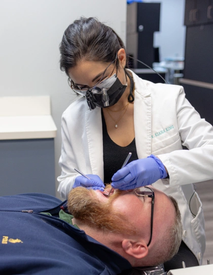 img-blvd-dentistry—orthodontics6 Healthcare professional in white coat and mask examining patient's face in medical clinic setting.
