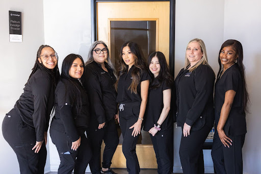 Seven women in black uniforms pose together in an indoor hallway setting.