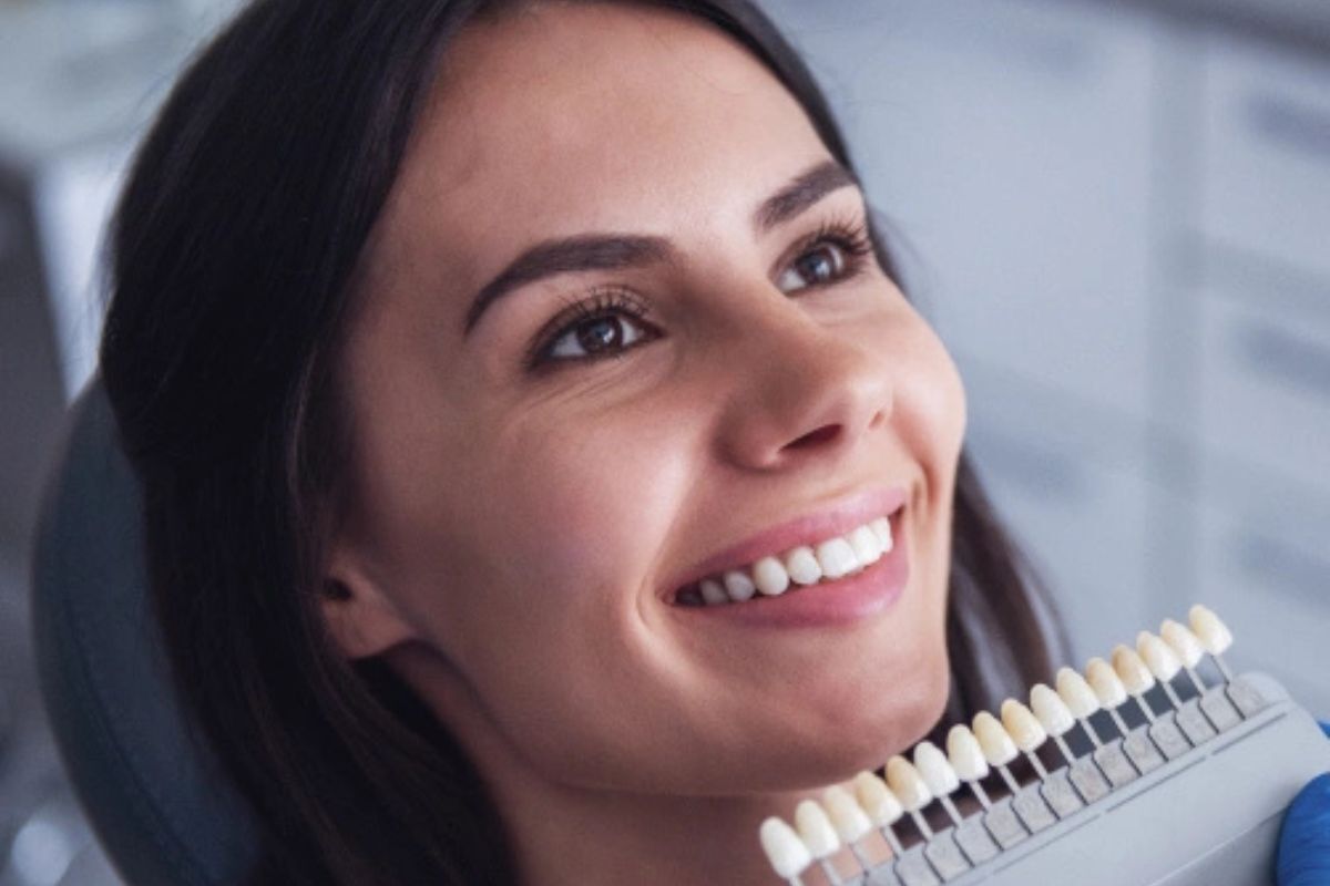 Woman smiling while holding a dental veneer shade guide showing tooth color options.