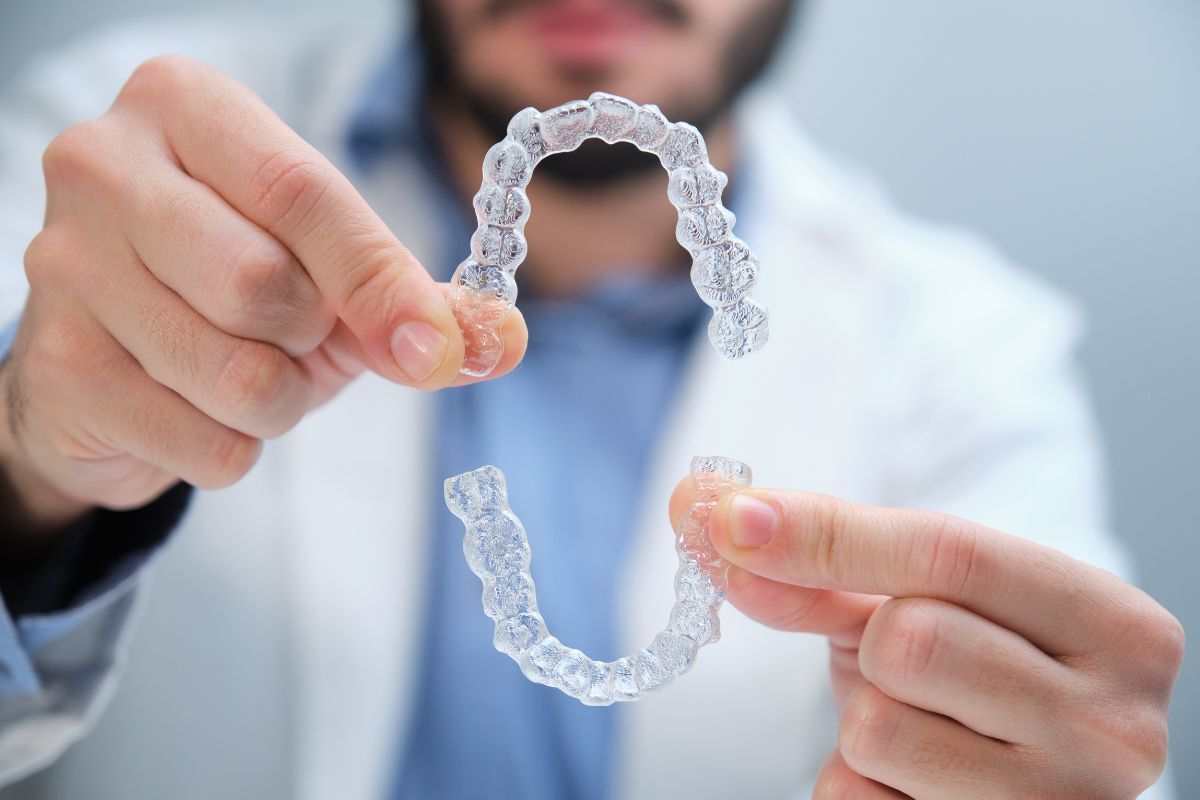 Houston orthodontist evaluating a patient’s tooth alignment and bite Orthodontist holding clear aligners for teeth straightening treatment in Fort Worth.